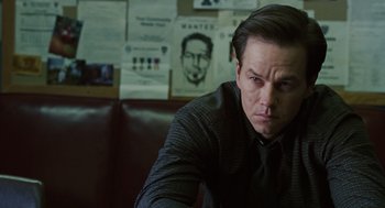 Movie still from “We Own the Night” (2007), directed by James Gray – A man sitting in front of a bunch of posters; Close Up shot, Over the shoulder angle