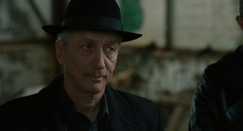 Movie still from “We Own the Night” (2007), directed by James Gray – An older man wearing a black hat and a black suit; Close Up shot, Over the shoulder angle