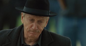 Movie still from “We Own the Night” (2007), directed by James Gray – An older man wearing a black hat and a black jacket; Close Up shot, Low angle