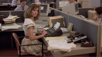 Movie still from “Weekend at Bernie's” (1989), directed by Ted Kotcheff – A woman sitting at a computer desk typing on a typewriter; Medium shot, High angle