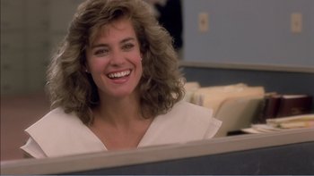 Movie still from “Weekend at Bernie's” (1989), directed by Ted Kotcheff – A woman sitting in an office cubicle smiling for the camera; Close Up shot, Over the shoulder angle