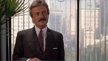Movie still from “Weekend at Bernie's” (1989), directed by Ted Kotcheff – A man in a suit and tie standing in front of a window; Medium shot, Low angle