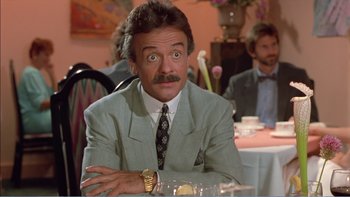 Movie still from “Weekend at Bernie's” (1989), directed by Ted Kotcheff – A man in a suit sitting at a dinner table; Close Up shot, Over the shoulder angle
