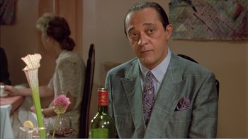 Movie still from “Weekend at Bernie's” (1989), directed by Ted Kotcheff – A man wearing a suit and tie holding a bottle of wine; Close Up shot, Over the shoulder angle