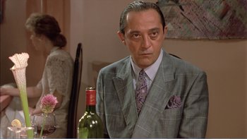Movie still from “Weekend at Bernie's” (1989), directed by Ted Kotcheff – A man in a suit and tie sitting in front of a bottle of wine; Close Up shot, Over the shoulder angle