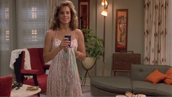 Movie still from “Weekend at Bernie's” (1989), directed by Ted Kotcheff – A woman holding a cell phone while standing in a living room; Medium shot, Over the shoulder angle
