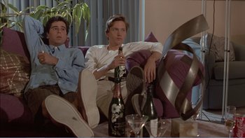 Movie still from “Weekend at Bernie's” (1989), directed by Ted Kotcheff – Two young men sitting on a couch drinking wine; Medium shot, Low angle