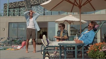 Movie still from “Weekend at Bernie's” (1989), directed by Ted Kotcheff – A man standing next to another man sitting on a chair; Wide shot, Low angle