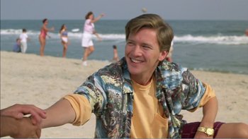 Movie still from “Weekend at Bernie's” (1989), directed by Ted Kotcheff – A man sitting on the beach with other people in the background; Medium shot, Low angle