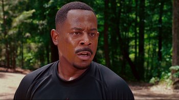 Movie still from “Welcome Home, Roscoe Jenkins” (2008), directed by Malcolm D. Lee – A person wearing a black t - shirt near a forest; Close Up shot, Over the shoulder angle