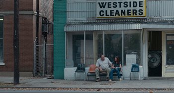 Movie still from “Welcome to the Rileys” (2010), directed by Jake Scott – A man and a woman sitting on a bench outside of a store; Wide shot, Over the shoulder angle