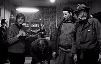Movie still from “Werckmeister Harmonies” (2000), directed by Ágnes Hranitzky – A man kneeling down in front of a group of people; Medium shot, Over the shoulder angle