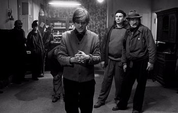 Movie still from “Werckmeister Harmonies” (2000), directed by Ágnes Hranitzky – A group of people standing around a room; Medium shot, Over the shoulder angle