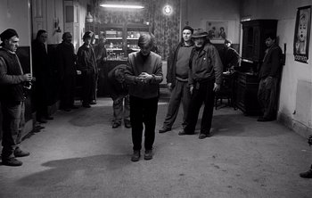 Movie still from “Werckmeister Harmonies” (2000), directed by Ágnes Hranitzky – A group of men standing around in a room; Wide shot, High angle