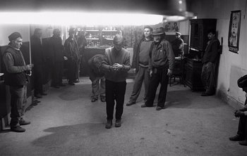 Movie still from “Werckmeister Harmonies” (2000), directed by Ágnes Hranitzky – A group of men standing around in a room; Wide shot, High angle