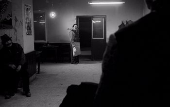 Movie still from “Werckmeister Harmonies” (2000), directed by Ágnes Hranitzky – A person standing in a room holding a phone; Wide shot, Over the shoulder angle