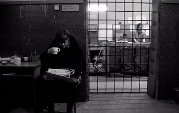 Movie still from “Werckmeister Harmonies” (2000), directed by Ágnes Hranitzky – A woman sitting in a chair holding a cup of coffee; Wide shot, Over the shoulder angle