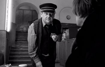 Movie still from “Werckmeister Harmonies” (2000), directed by Ágnes Hranitzky – A man wearing a hat and holding a cigarette; Medium shot, Over the shoulder angle