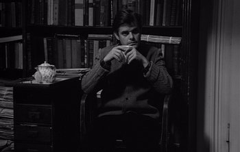 Movie still from “Werckmeister Harmonies” (2000), directed by Ágnes Hranitzky – A man sitting in front of a book shelf in a chair; Medium shot, Low angle