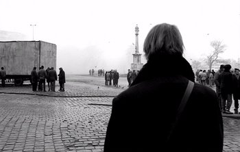 Movie still from “Werckmeister Harmonies” (2000), directed by Ágnes Hranitzky – A group of people standing on a cobblestone street; Medium shot, Over the shoulder angle