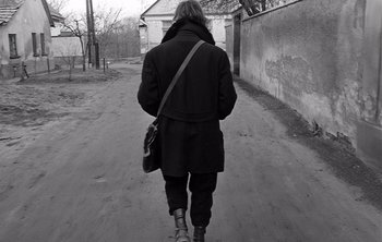 Movie still from “Werckmeister Harmonies” (2000), directed by Ágnes Hranitzky – A person walking down a street holding a purse; Medium shot, Low angle