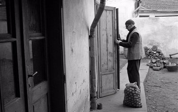 Movie still from “Werckmeister Harmonies” (2000), directed by Ágnes Hranitzky – A man standing next to an open door on a sidewalk; Wide shot, Low angle