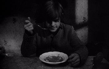 Movie still from “Werckmeister Harmonies” (2000), directed by Ágnes Hranitzky – A person sitting at a table with a plate of food in front of them; Medium shot, High angle