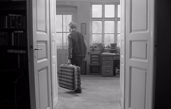 Movie still from “Werckmeister Harmonies” (2000), directed by Ágnes Hranitzky – A person with a suitcase walking through a room; Wide shot, High angle