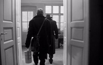 Movie still from “Werckmeister Harmonies” (2000), directed by Ágnes Hranitzky – Two people are walking through a doorway; Medium shot, Low angle