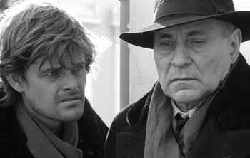 Movie still from “Werckmeister Harmonies” (2000), directed by Ágnes Hranitzky – Two men standing next to each other in front of a building; Close Up shot, Over the shoulder angle