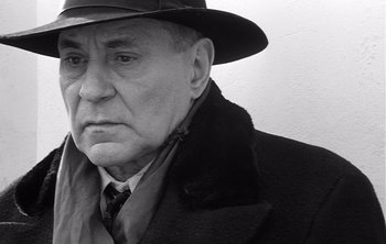 Movie still from “Werckmeister Harmonies” (2000), directed by Ágnes Hranitzky – An older man wearing a coat and a hat; Close Up shot, Low angle