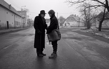 Movie still from “Werckmeister Harmonies” (2000), directed by Ágnes Hranitzky – Two men standing on a street corner talking to each other; Medium shot, Over the shoulder angle