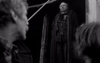 Movie still from “Werckmeister Harmonies” (2000), directed by Ágnes Hranitzky – An old man standing in front of a group of people; Medium shot, Over the shoulder angle