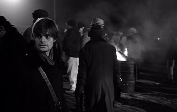 Movie still from “Werckmeister Harmonies” (2000), directed by Ágnes Hranitzky – A group of people standing next to a fire pit at night; Medium shot, Over the shoulder angle
