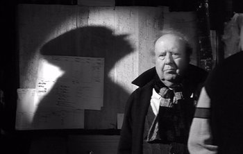 Movie still from “Werckmeister Harmonies” (2000), directed by Ágnes Hranitzky – An old man standing in front of a bunch of papers; Close Up shot, Low angle