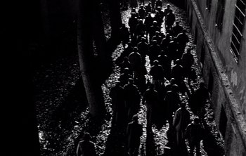 Movie still from “Werckmeister Harmonies” (2000), directed by Ágnes Hranitzky – A black and white photo of a group of people walking down a path; Extreme Wide shot, High angle