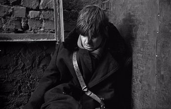 Movie still from “Werckmeister Harmonies” (2000), directed by Ágnes Hranitzky – A man sitting on the side of a building; Close Up shot, Low angle