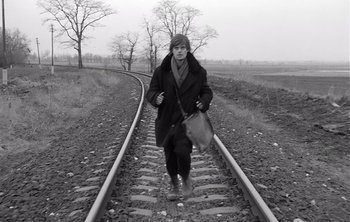 Movie still from “Werckmeister Harmonies” (2000), directed by Ágnes Hranitzky – A person walking on train tracks holding a bag; Wide shot, High angle