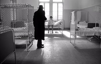 Movie still from “Werckmeister Harmonies” (2000), directed by Ágnes Hranitzky – A man wearing a hat and a long coat standing in front of a child; Wide shot, Low angle