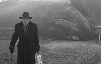 Movie still from “Werckmeister Harmonies” (2000), directed by Ágnes Hranitzky – An old man in a hat and coat holding a bottle; Medium shot, Low angle