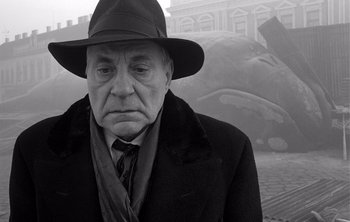 Movie still from “Werckmeister Harmonies” (2000), directed by Ágnes Hranitzky – An older man in a hat and a black coat; Close Up shot, Low angle