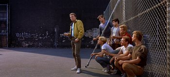 Movie still from “West Side Story” (1961), directed by Jerome Robbins – A group of young men standing on top of a basketball court; Wide shot, Over the shoulder angle