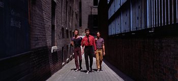Movie still from “West Side Story” (1961), directed by Jerome Robbins – Three young men are walking down a brick alley; Wide shot, High angle