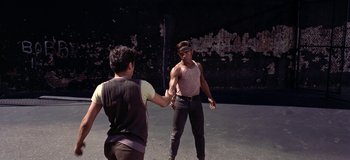 Movie still from “West Side Story” (1961), directed by Jerome Robbins – Two young men are holding hands in an outdoor setting; Medium shot, Over the shoulder angle
