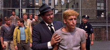 Movie still from “West Side Story” (1961), directed by Jerome Robbins – A man in a suit and a hat standing next to a man in a gray shirt; Medium shot, Over the shoulder angle