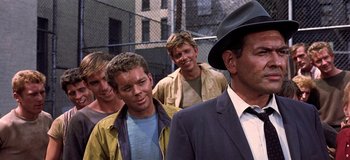 Movie still from “West Side Story” (1961), directed by Jerome Robbins – A group of men standing next to each other in front of a chain link fence; Close Up shot, Over the shoulder angle