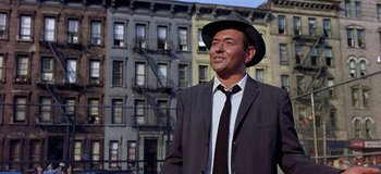 Movie still from “West Side Story” (1961), directed by Jerome Robbins – A man wearing a hat and a suit standing in front of a building; Medium shot, Low angle