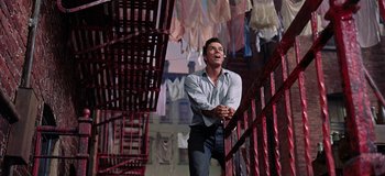Movie still from “West Side Story” (1961), directed by Jerome Robbins – A man standing on top of a staircase next to a bunch of clothes; Medium shot, Low angle