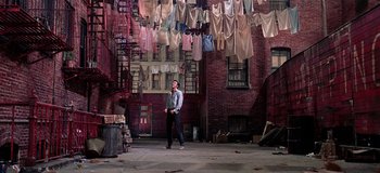Movie still from “West Side Story” (1961), directed by Jerome Robbins – A man standing in front of a brick building with clothes hanging from the ceiling; Wide shot, Low angle