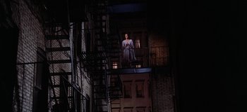Movie still from “West Side Story” (1961), directed by Jerome Robbins – A woman standing on a balcony in a building; Wide shot, High angle